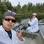 Two woman in a boat on a lake surrounded by woods.