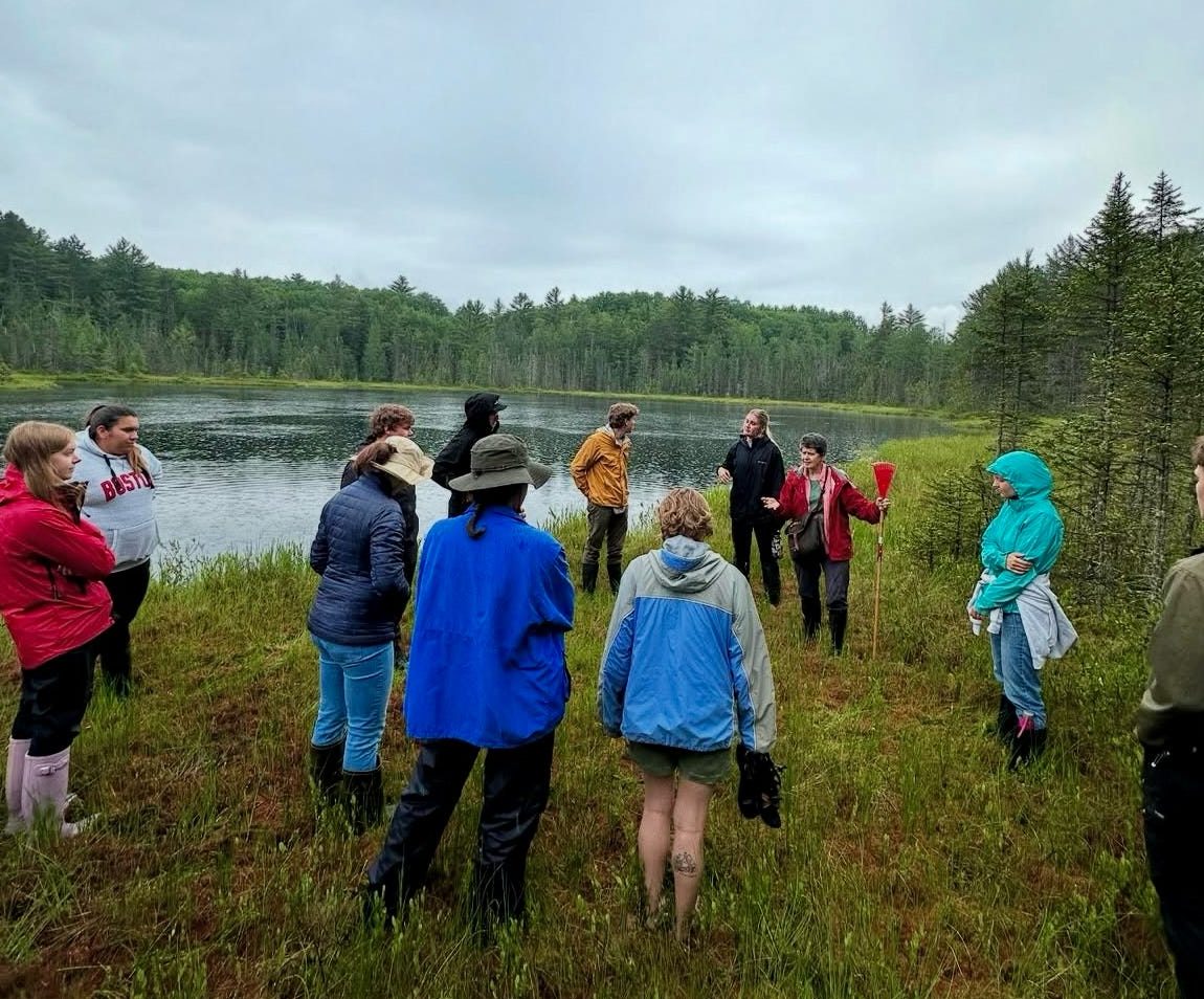 Students on a field trip stand near a lake.