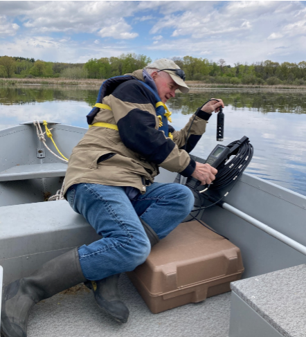 A person is sitting on a boat on a river using a temperature and dissolved oxygen sensor probe.